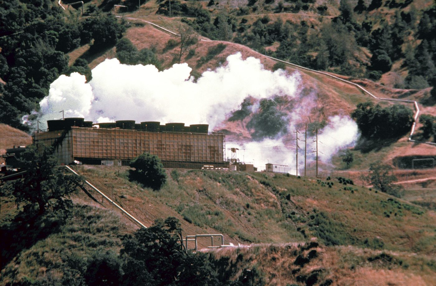 A geothermal power plant in a hilly landscape, with steam and industrial buildings.